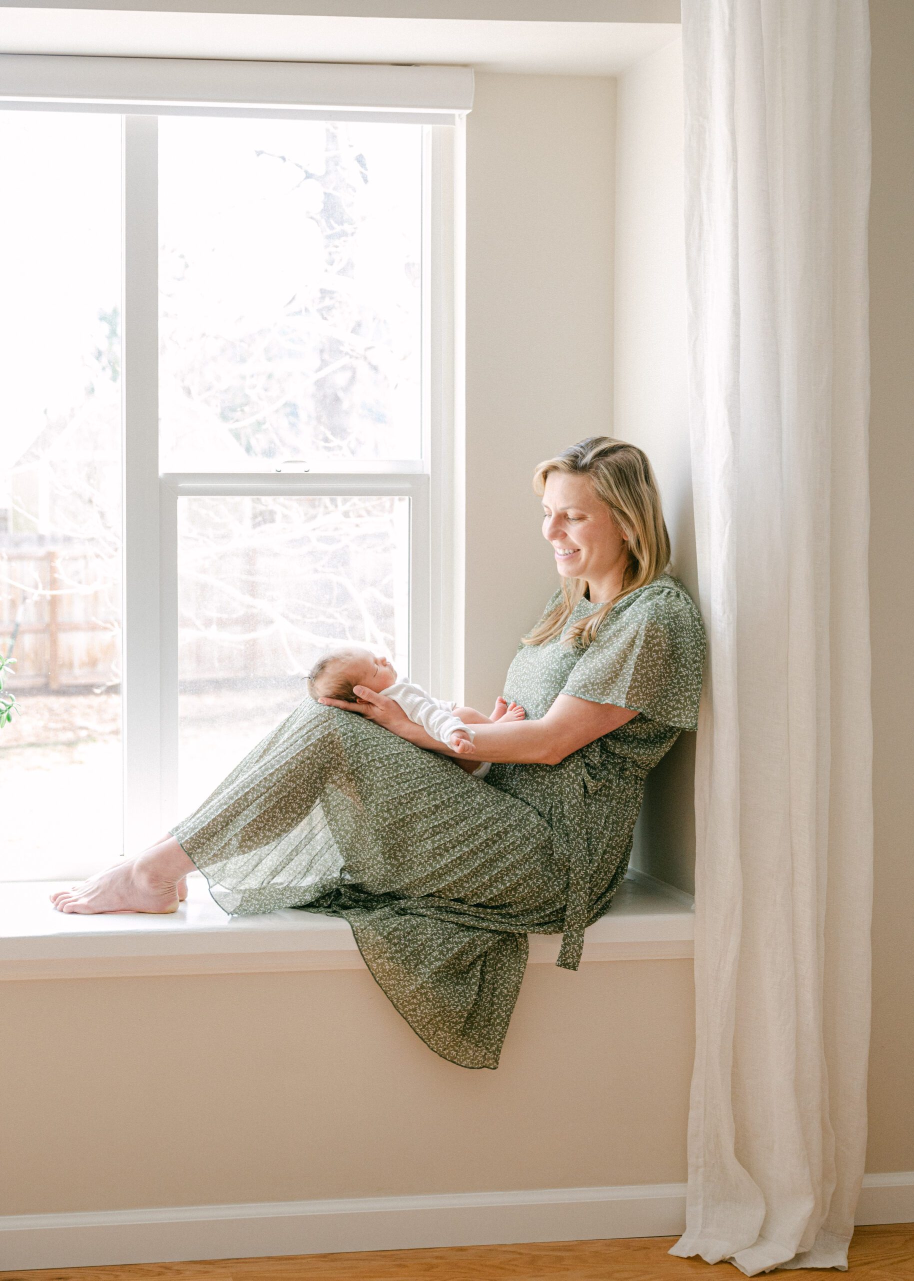 Mom sitting in a window sill looking at her newborn baby.