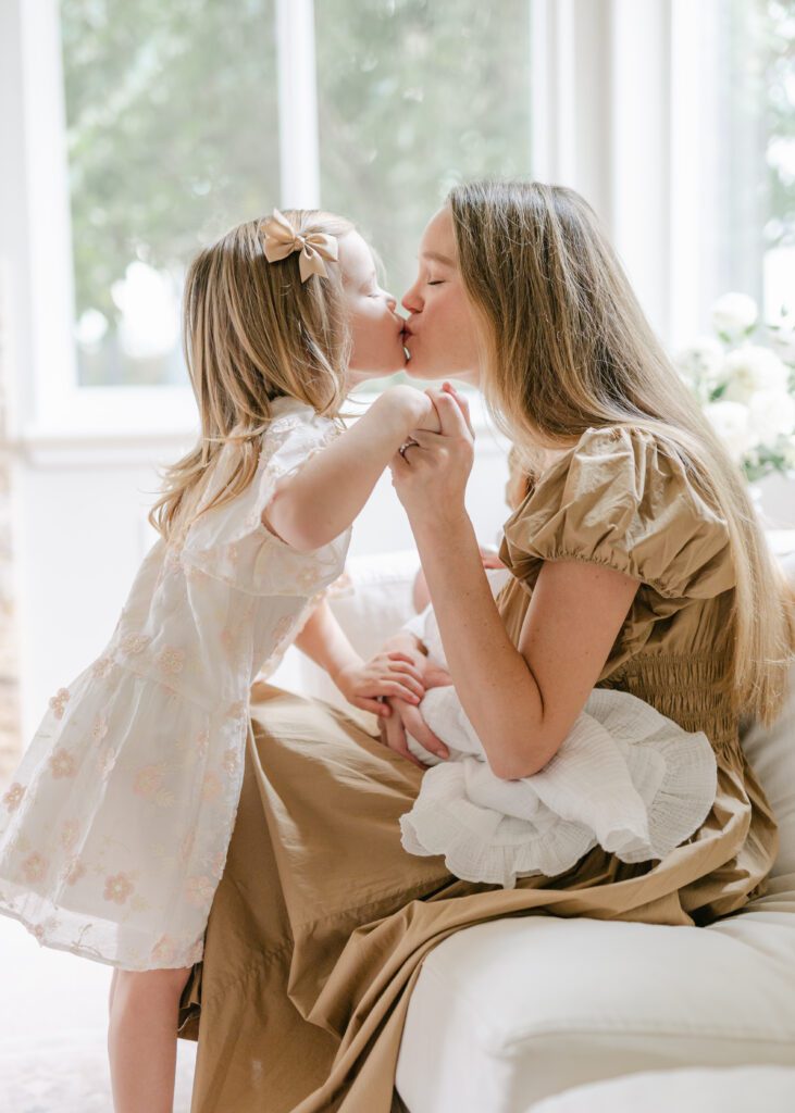 Mom and toddler girl sharing a sweet kiss while the mom holds a newborn baby.  Photo by Denver photographer Maegan R Photography