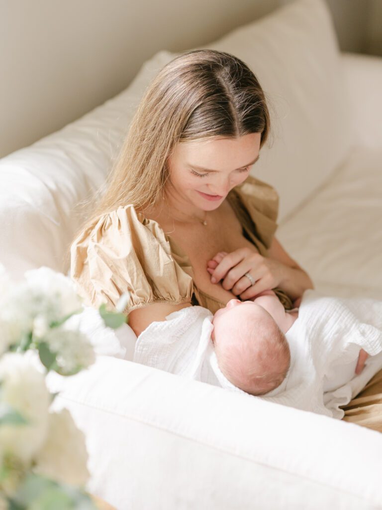 A picture peering in over fresh white flowers of a mom smiling down at her newborn baby.  Photo by Denver photographer Maegan R Photography