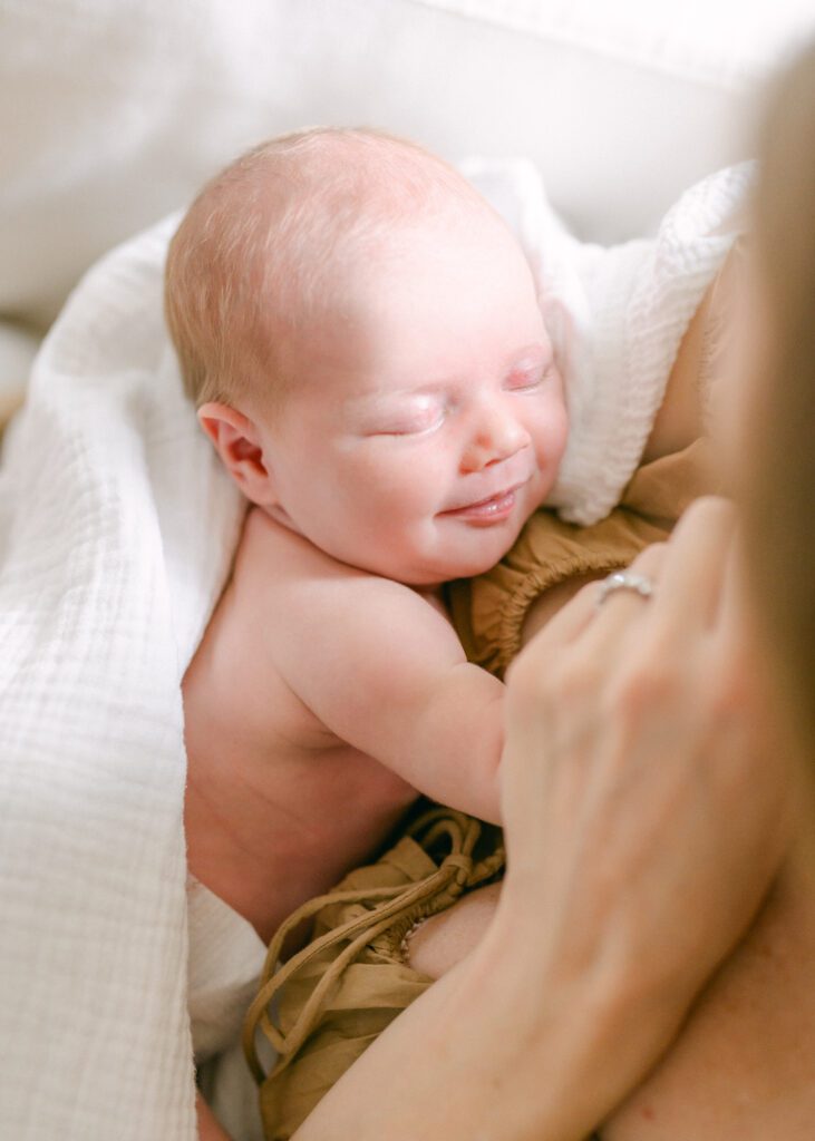 Photograph of a newborn baby smiling while they're being held in their mother's arms. Photo by Denver photographer Maegan R Photography