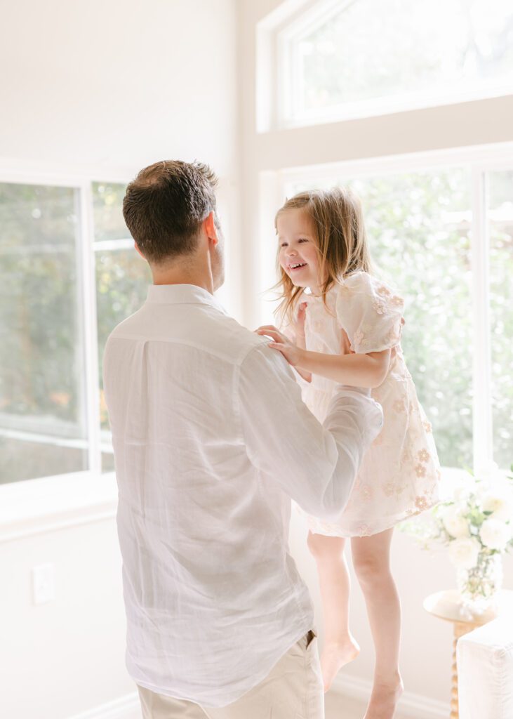 Dad dancing with his toddler daughter, swinging her in the air while she giggles. Photo by Denver photographer Maegan R Photography