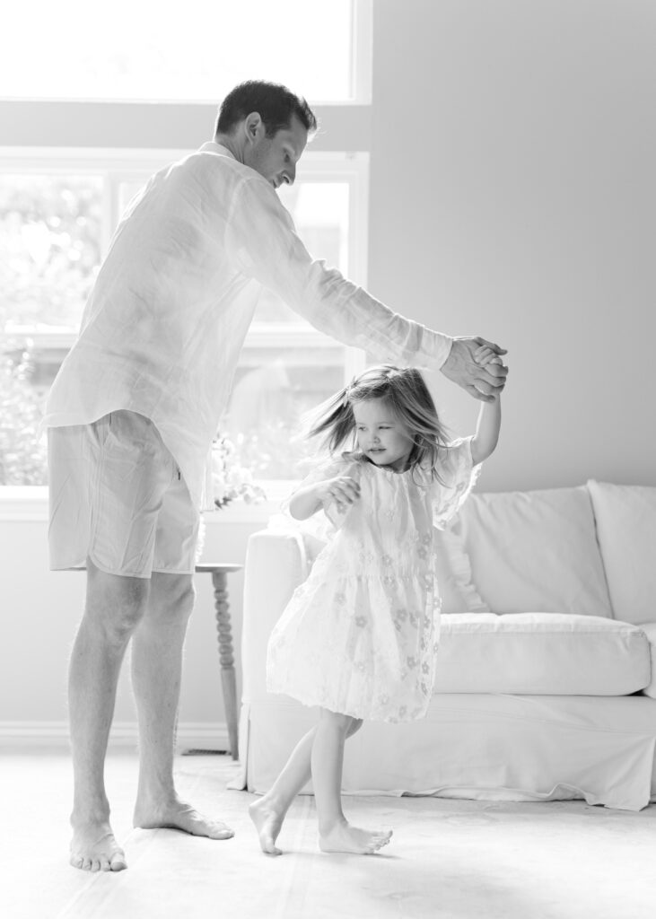 Black and white image of a dad twirling his daughter in a flowy dress. Photo by Denver photographer Maegan R Photography