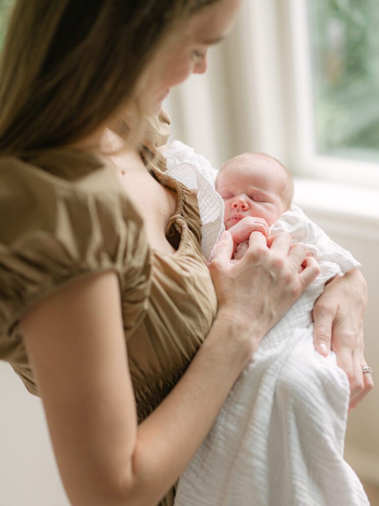 Mom holding a newborn baby looking down at her while the baby holds the moms finger and sleeps peacefully. Photograph by Maegan R Photography. 