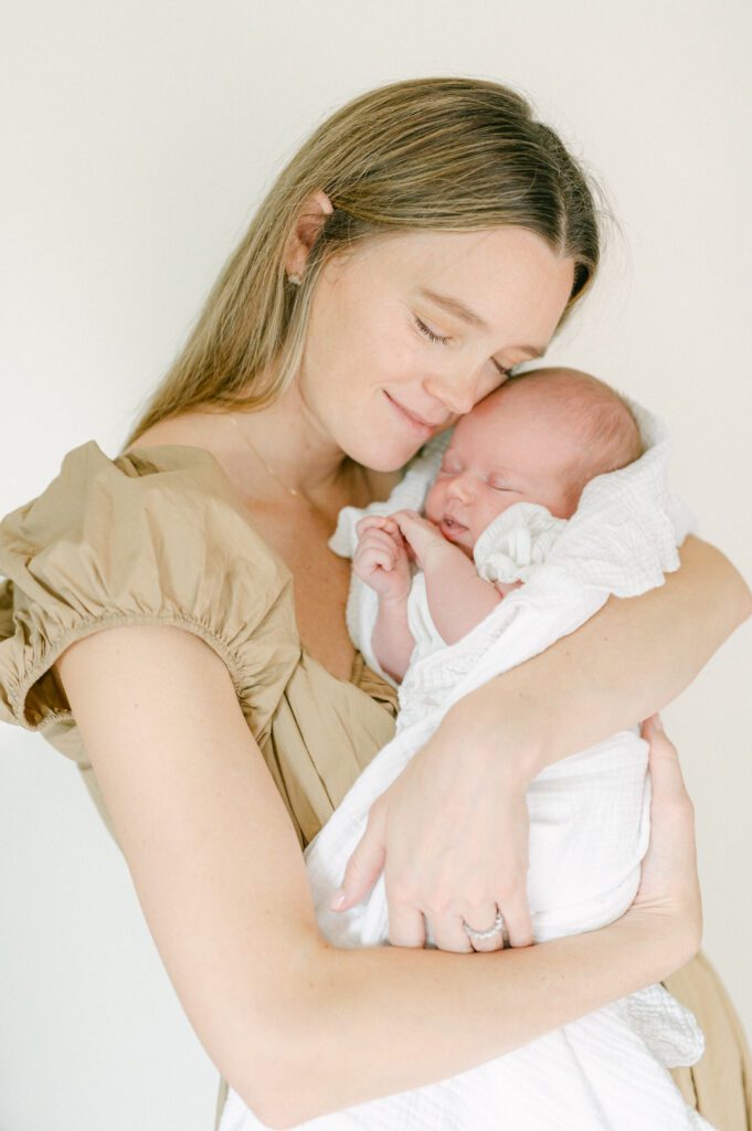 Mom holding and snuggling her newborn baby wrapped in a soft white blanket.  Photograph by Maegan R Photography. 