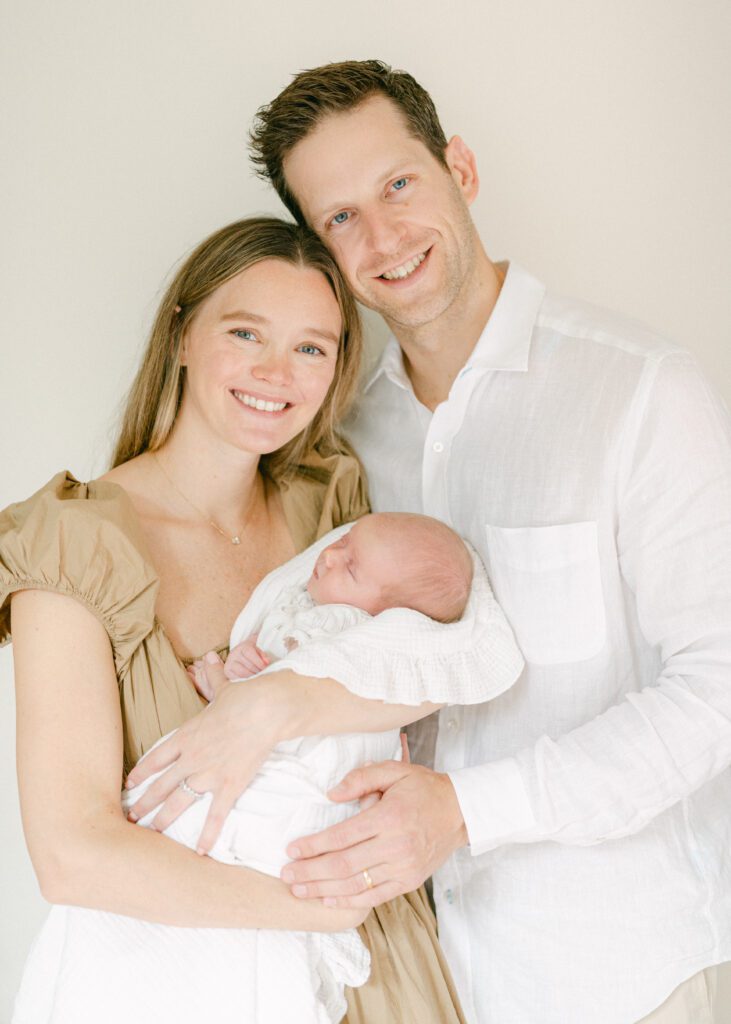 A mom and dad smiling and snuggling while they hold their newborn baby.  Photograph by Maegan R Photography. 