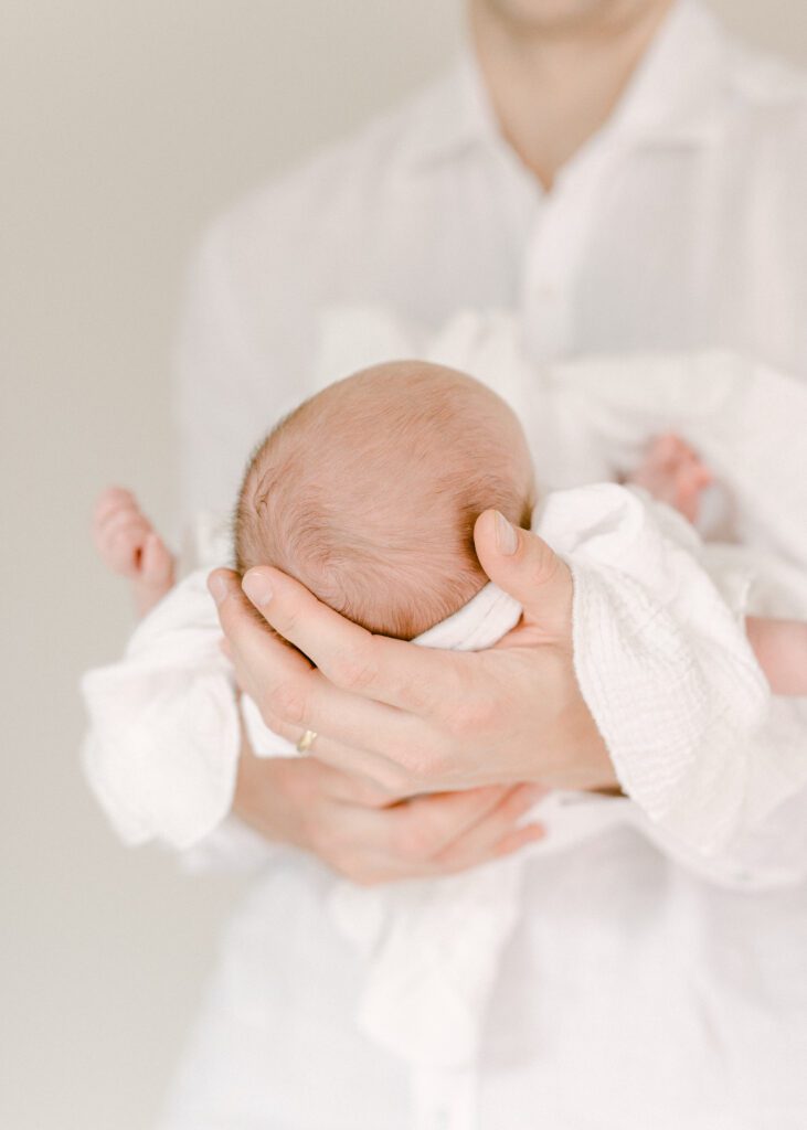 Photo of a man holding his newborn baby, dressing in classic white outfits. Photograph by Maegan R Photography. 