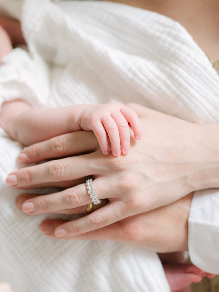 Sweet photograph of a man and woman holding a newborn baby's hand. Photograph by Maegan R Photography. 