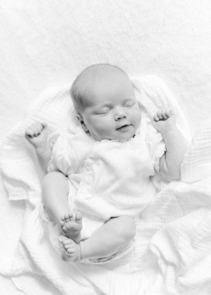 Black and white photo of a baby smiling and sleeping on a classic white blanket.  Photograph by Maegan R Photography. 